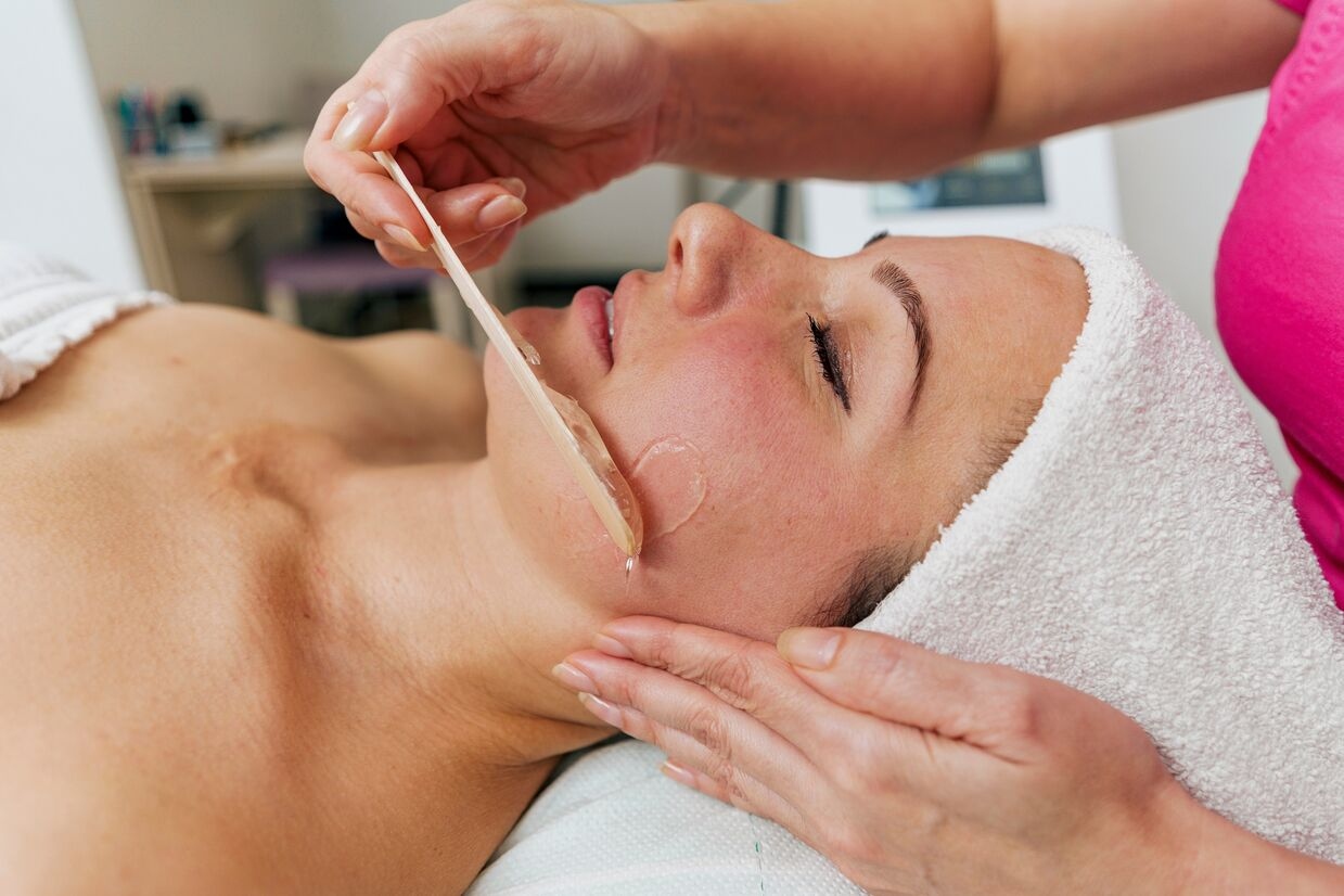 Close-up of a woman getting a gel or wax applied to her jawline during an Age Firming Facial beauty treatment.