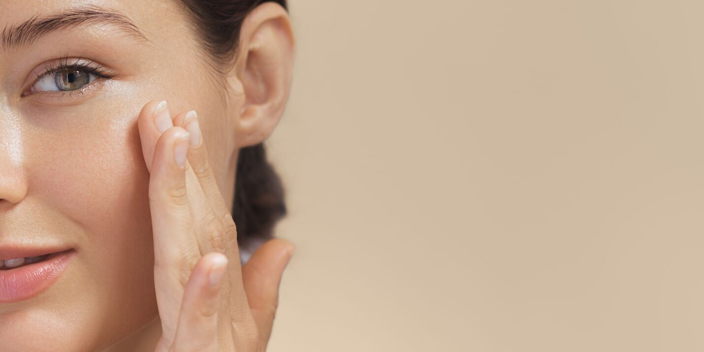 A close-up of a woman gently applying a skincare product to her cheek as part of an Age Firming Facial.