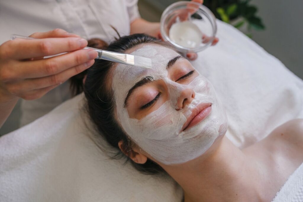 A close-up of a woman receiving a facial mask application during an Age Firming Facial treatment.