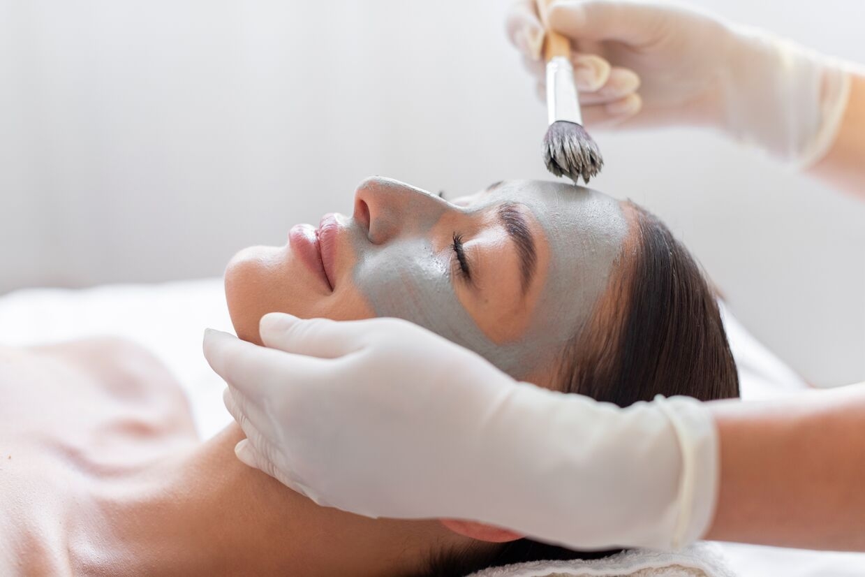 Woman receiving a facial mask treatment applied with a brush by a professional.