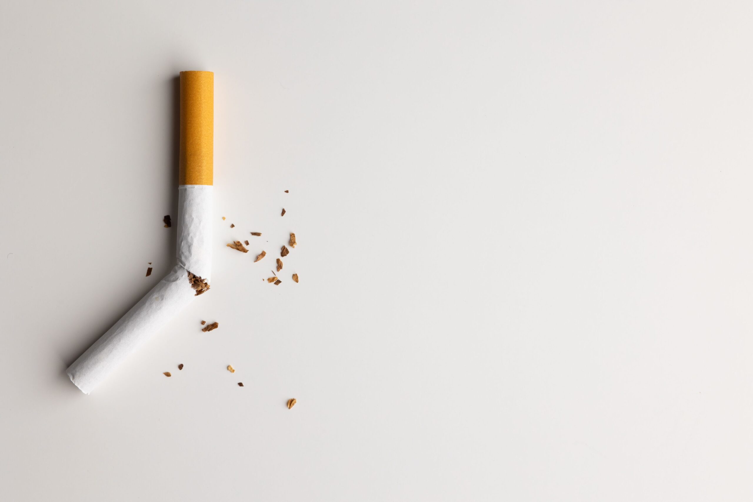 A bent and broken cigarette with scattered tobacco on a clean surface, representing the decision to quit smoking.