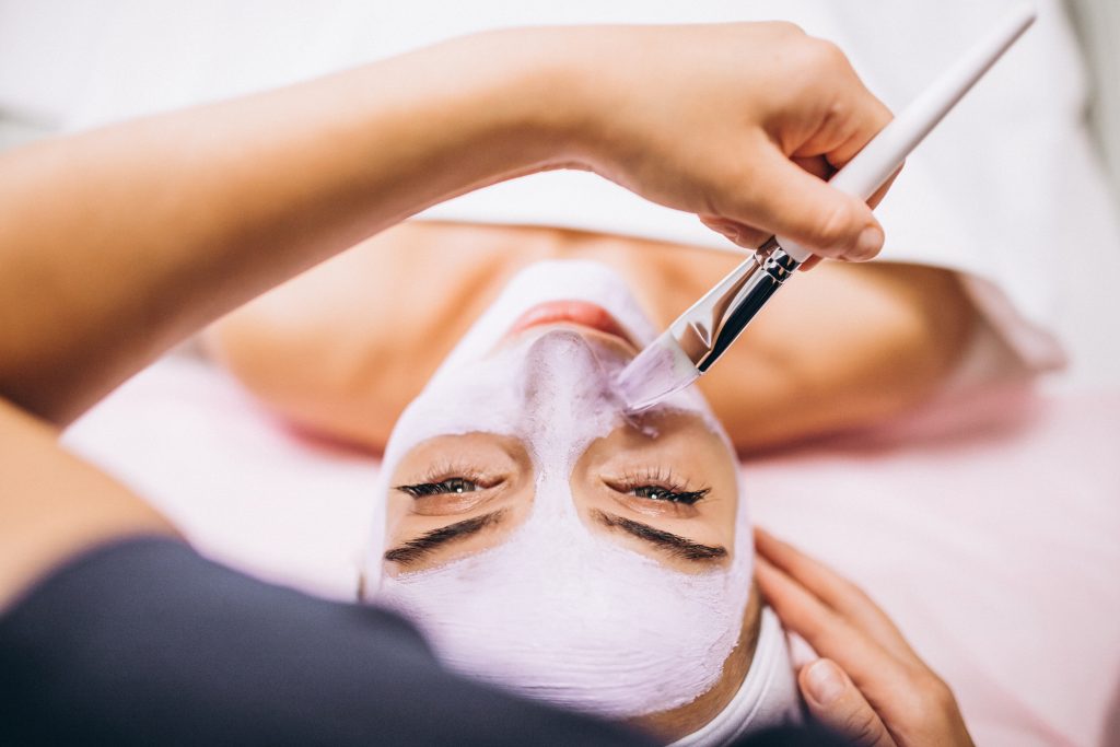 cosmetologist applying mask on a face of client in a beauty salon
