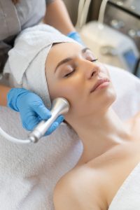 young woman lying on cosmetologist's table during rejuvenation procedure. cosmetologist take care about neck and face skin youthfull and wellness. hardware face cleaning procedure